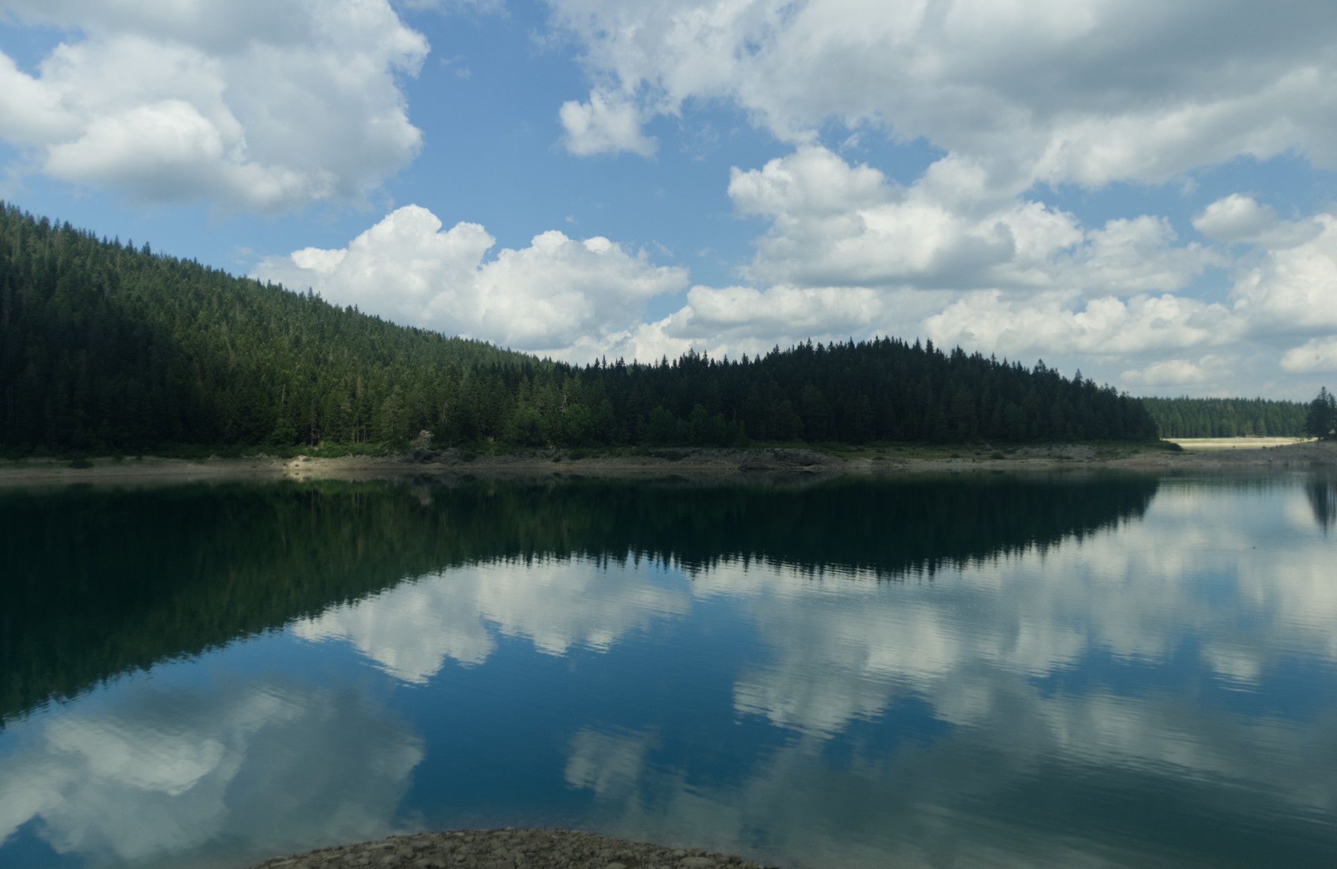 A panoramic photo of a lake with the far shore perfectly reflected in its waters