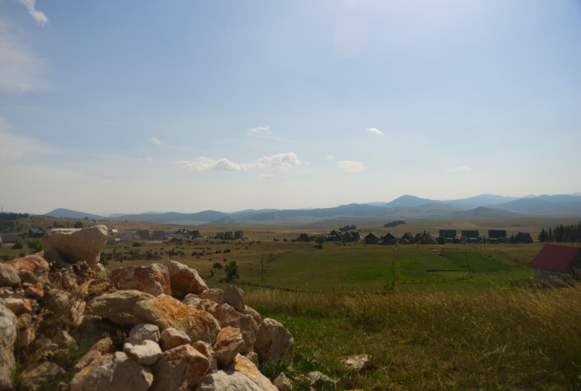 A photo of a valley with some houses and huts visible, and a pile of orange-red stone in the foreground