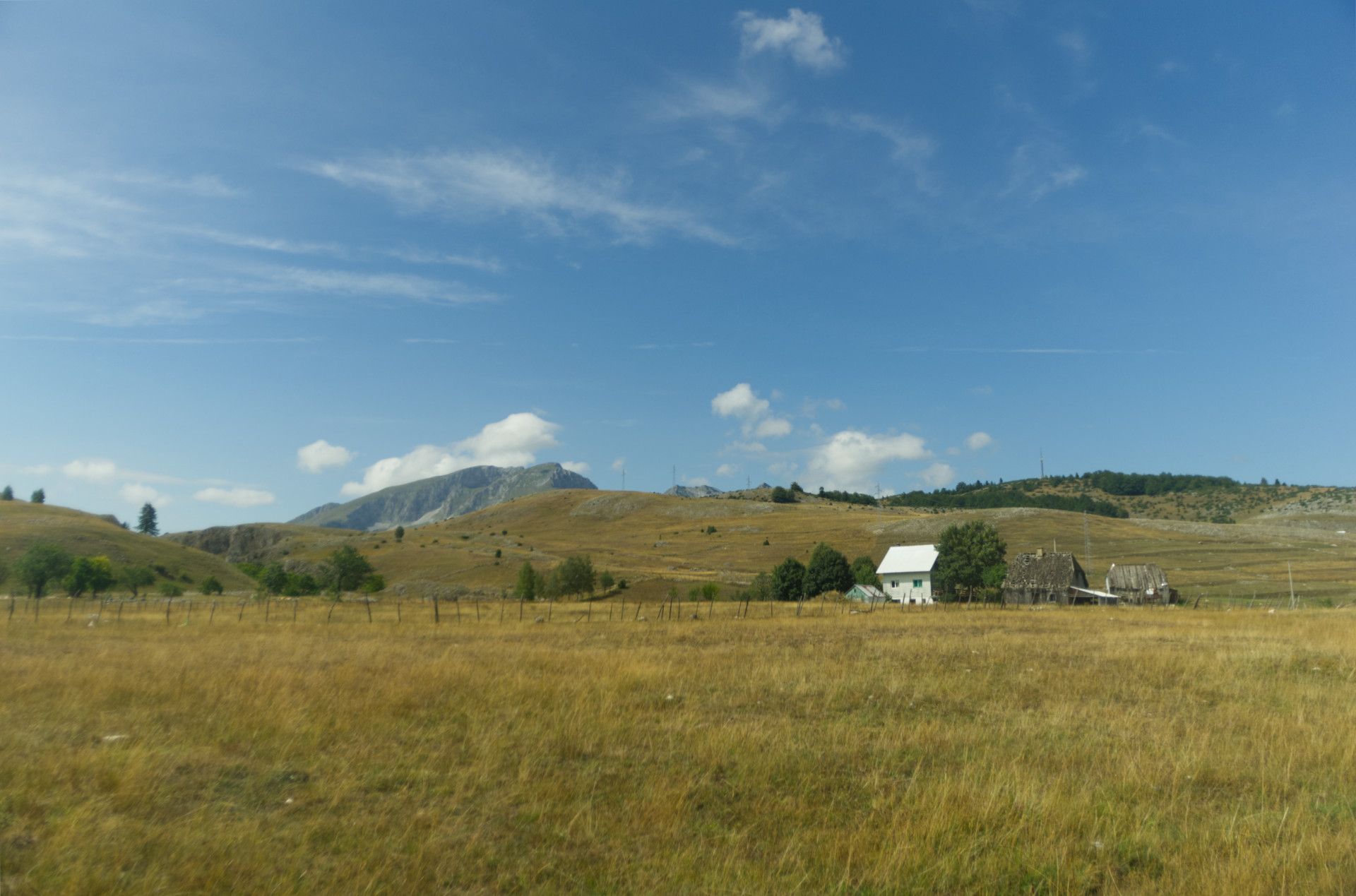 A photo of a hilly field with a ridge behind it, some buildings are visible in the middle distance
